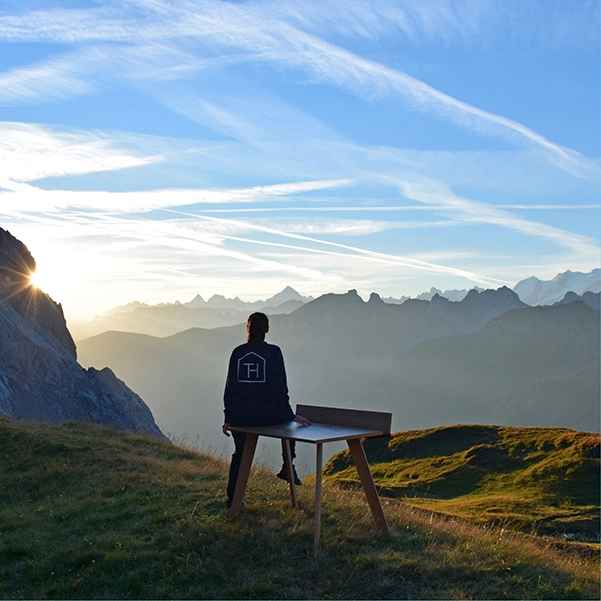 photo d'un coucher de soleil sur des montagne avec en premier plan un bureau posé sur l'herbe